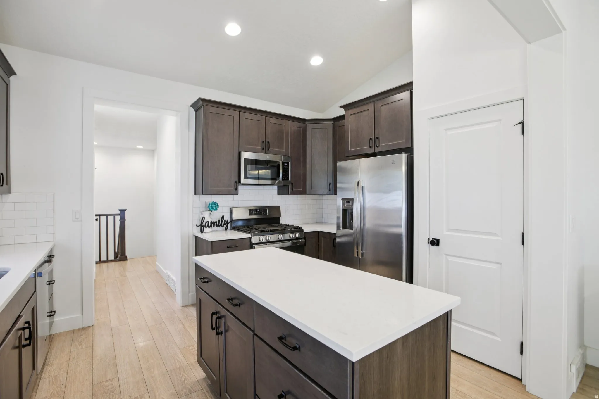 Kitchen with dark wood finish cabinetry, stainless steel appliances, light wood-style floors, a kitchen island, and tasteful backsplash