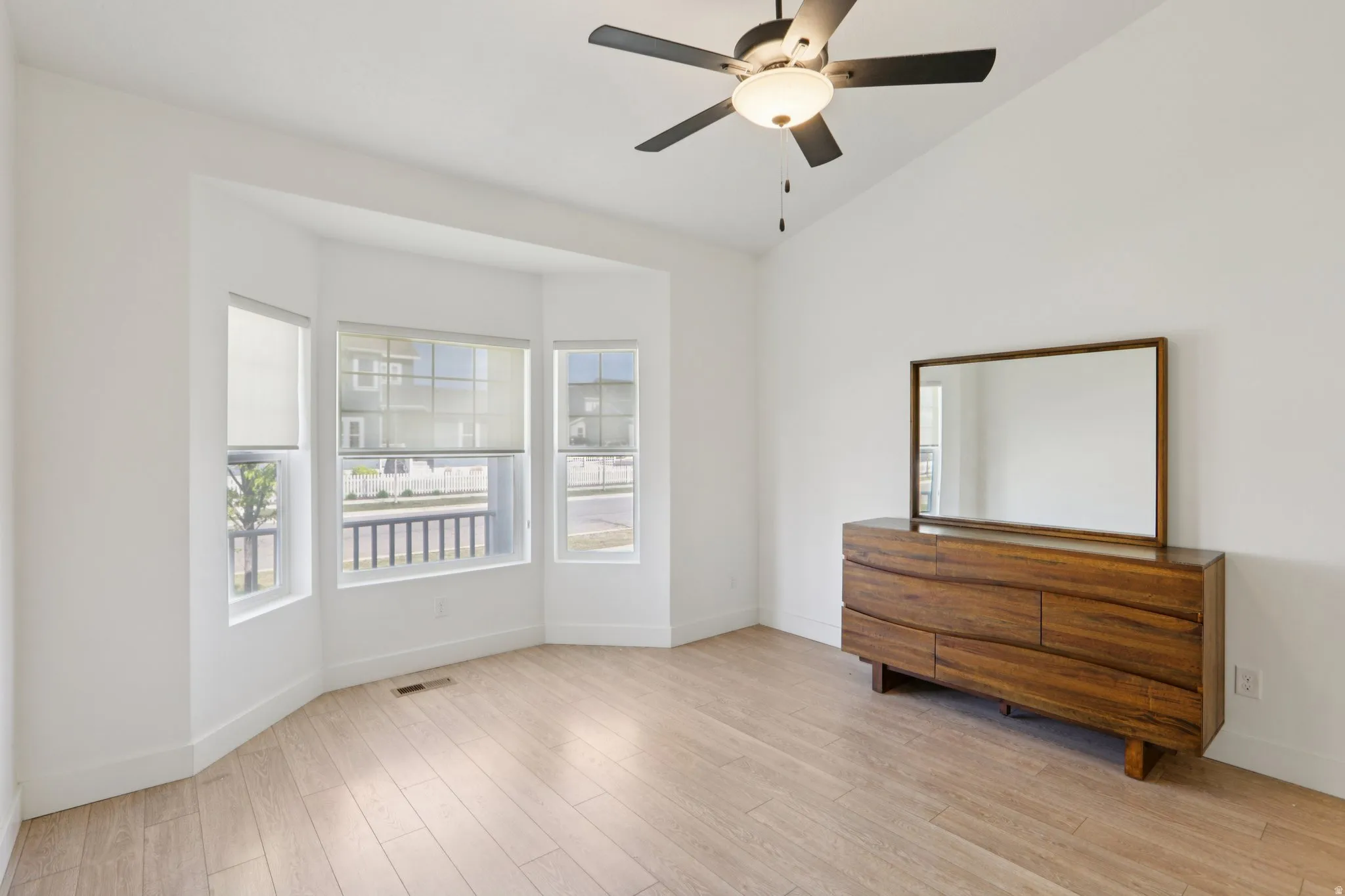 Empty room featuring ceiling fan, vaulted ceiling, and light wood-type flooring