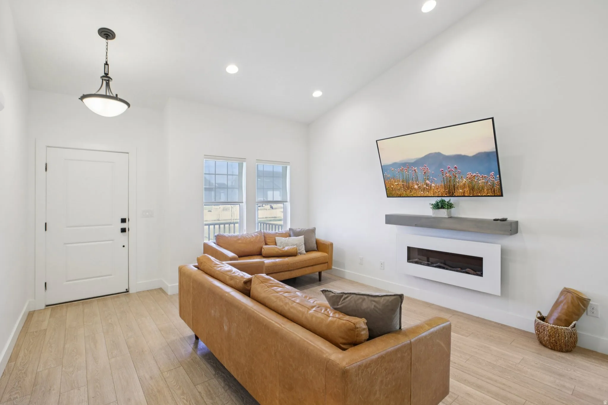 Living area with a glass covered fireplace, light wood finished floors, vaulted ceiling, and recessed lighting