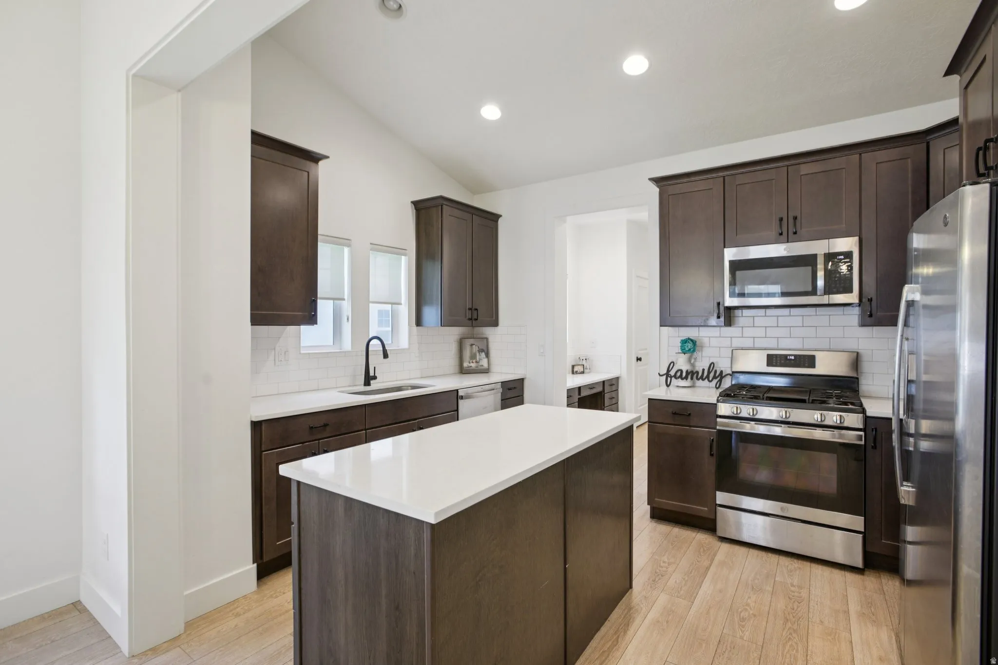 Kitchen featuring dark wood finish cabinetry, stainless steel appliances, a kitchen island, light wood finished floors, and vaulted ceiling