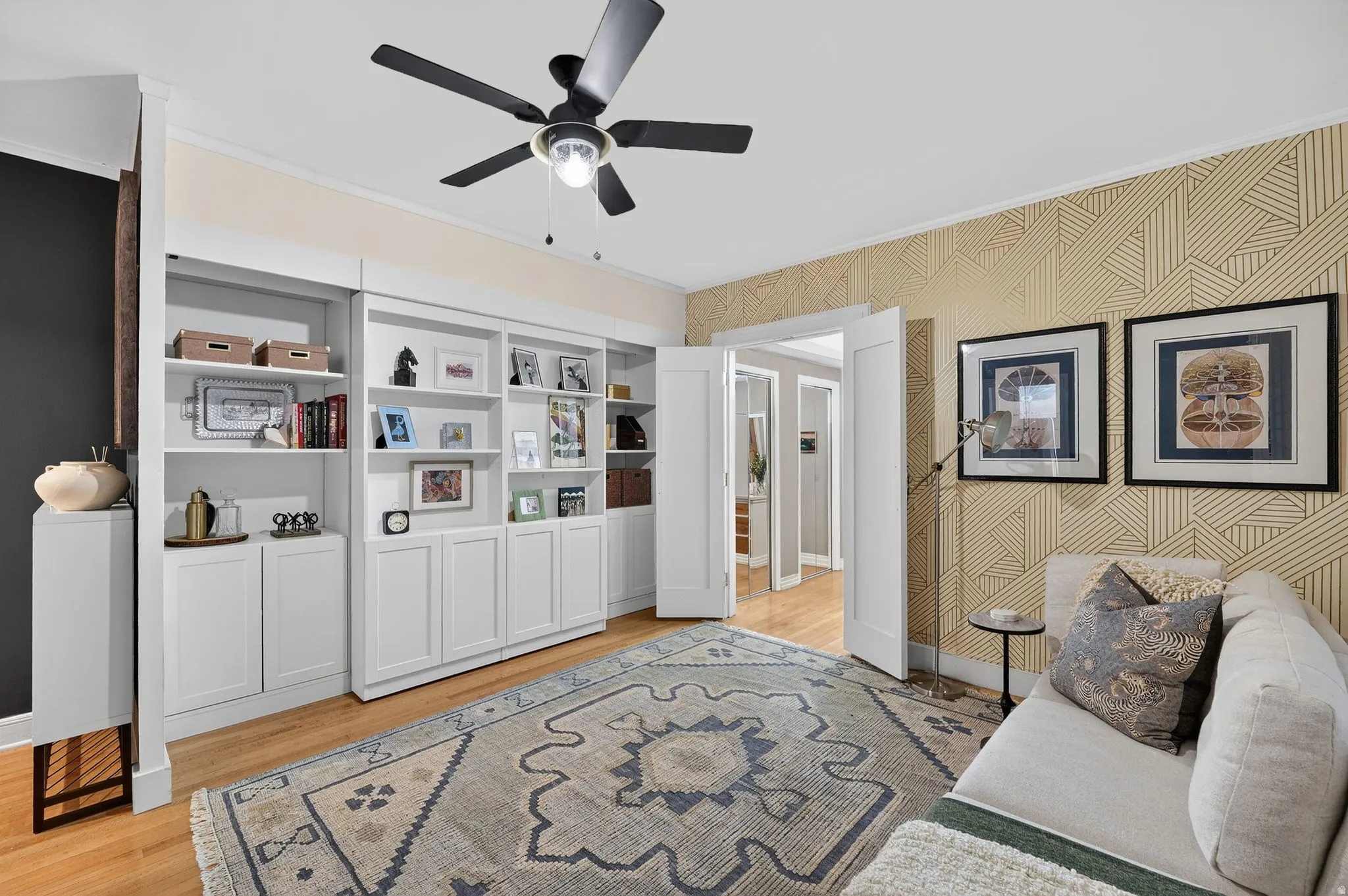 Room featuring extensive built-in white cabinetry and shelving, hardwood flooring, and a ceiling fan with light fixture