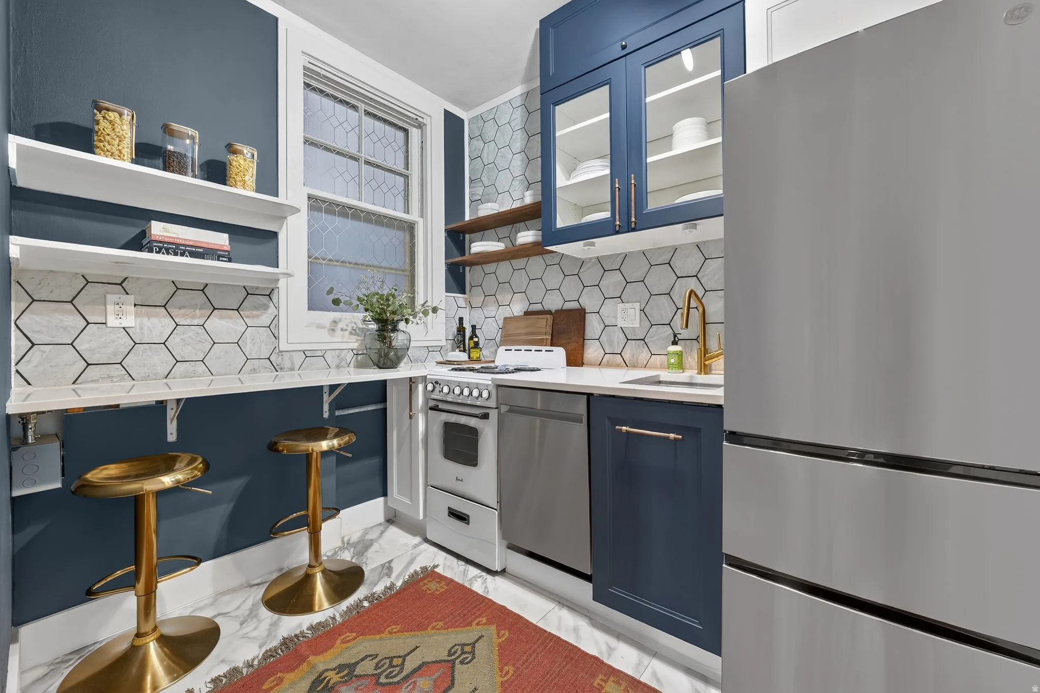 Kitchen featuring stainless steel appliances, blue cabinetry, light stone countertops, glass insert cabinets, and tasteful backsplash