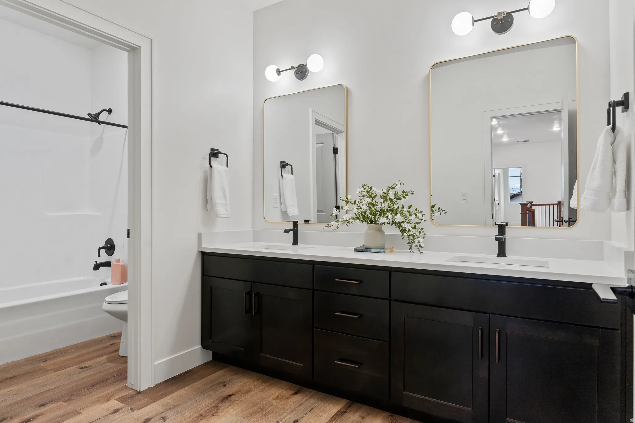 Bathroom featuring double vanity, light wood-style flooring, and bathing tub / shower combination