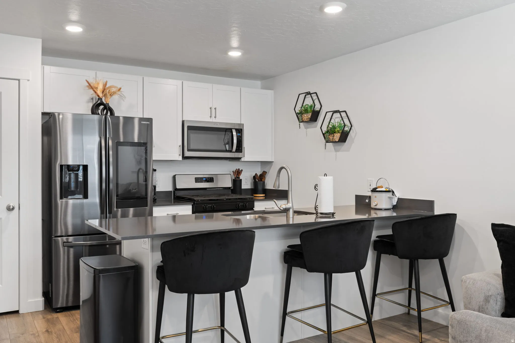 Kitchen featuring a breakfast bar area, stainless steel appliances, a peninsula, white cabinetry, and light wood finished floors