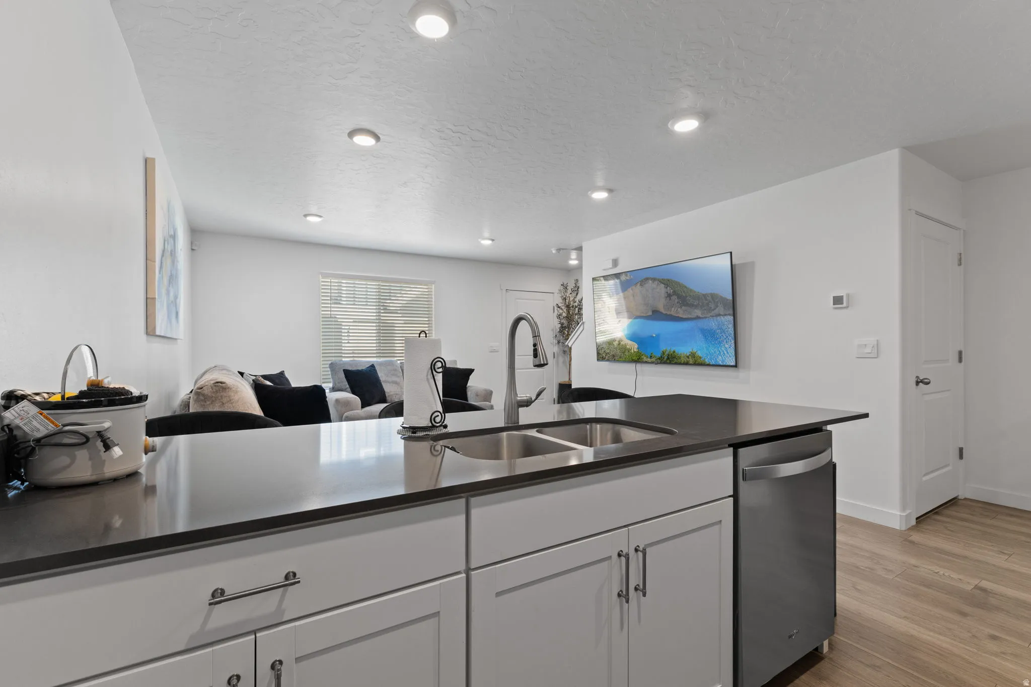 Kitchen featuring stainless steel dishwasher, light wood-style flooring, a textured ceiling, open floor plan, and white cabinetry