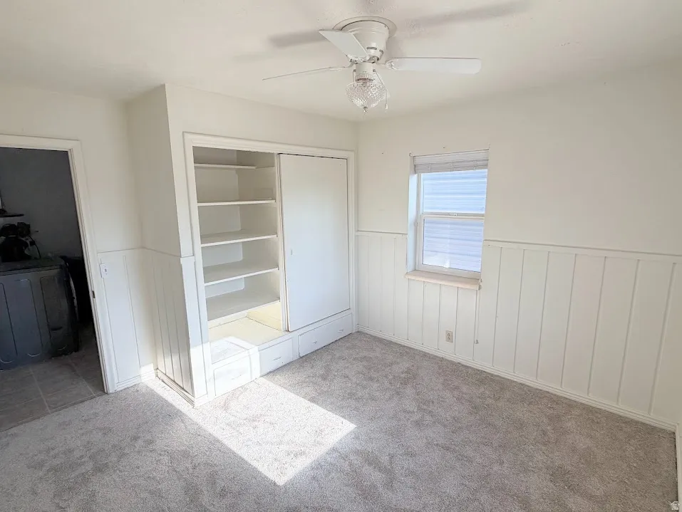 Room featuring light gray carpeting, white board-and-batten wainscoting, and a white ceiling fan with a clear glass light fixture