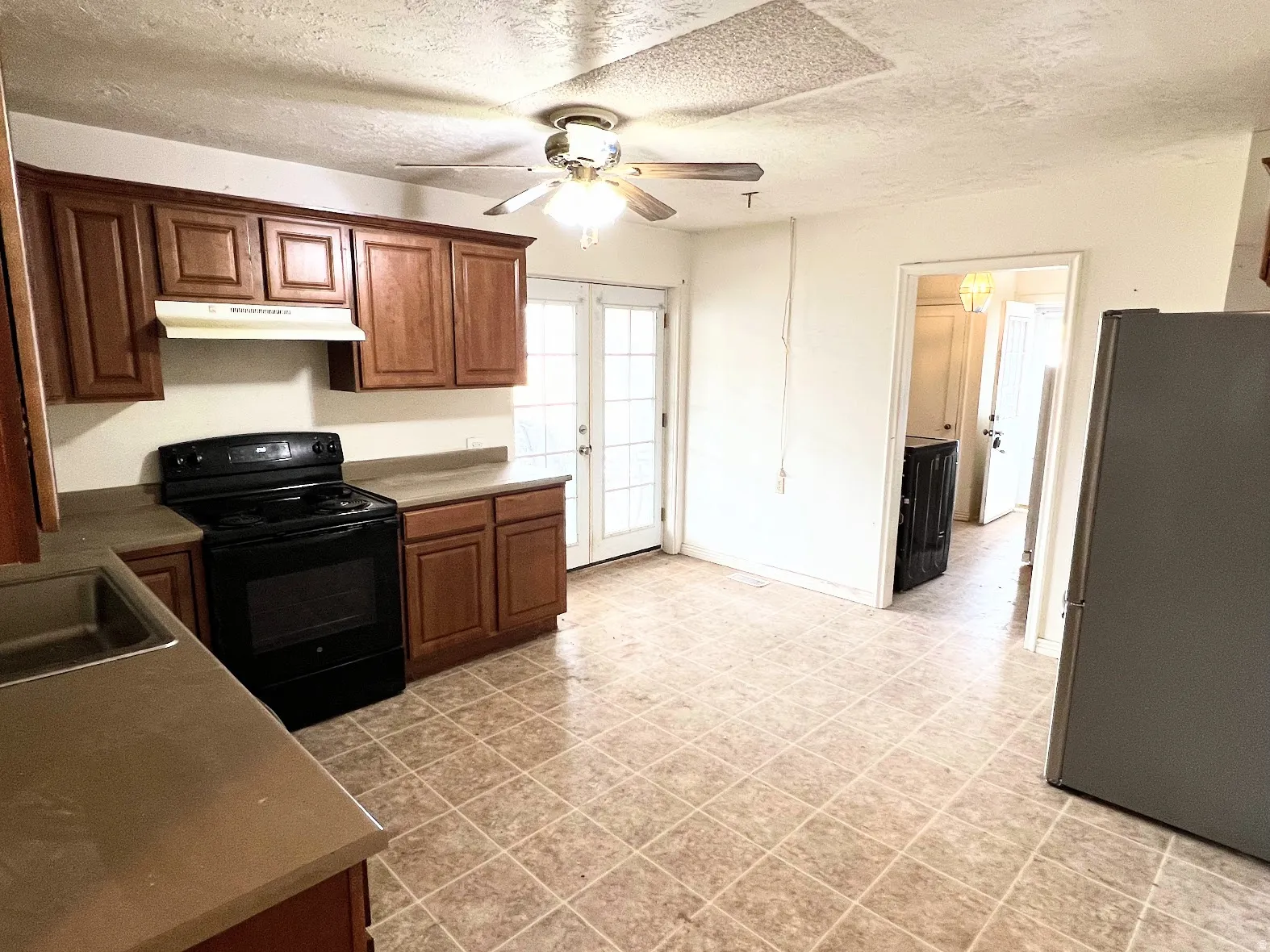 Kitchen with black range with electric stovetop, freestanding refrigerator, ceiling fan, a textured ceiling, and dark countertops