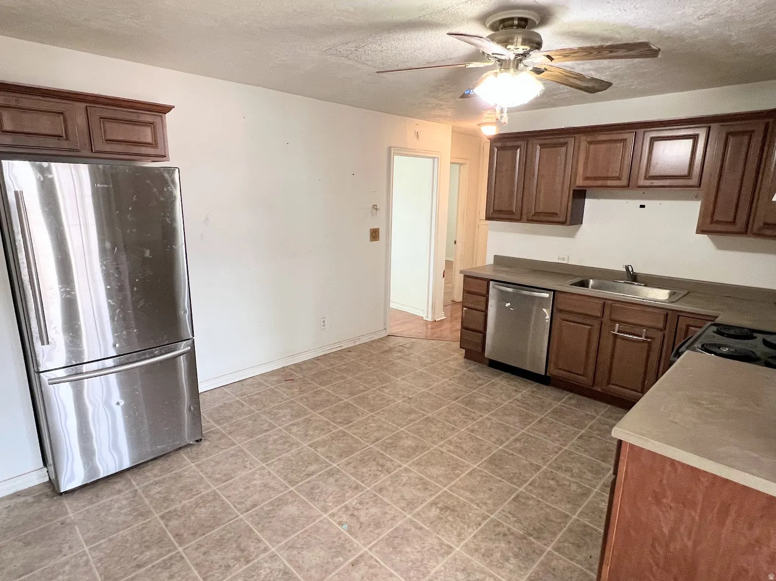 Kitchen with stainless steel appliances, ceiling fan, a textured ceiling, and wood finish cabinetry