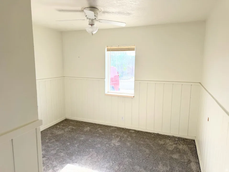 Room featuring textured carpet, board and batten wainscoting, a single window, and a ceiling fan with integrated lighting