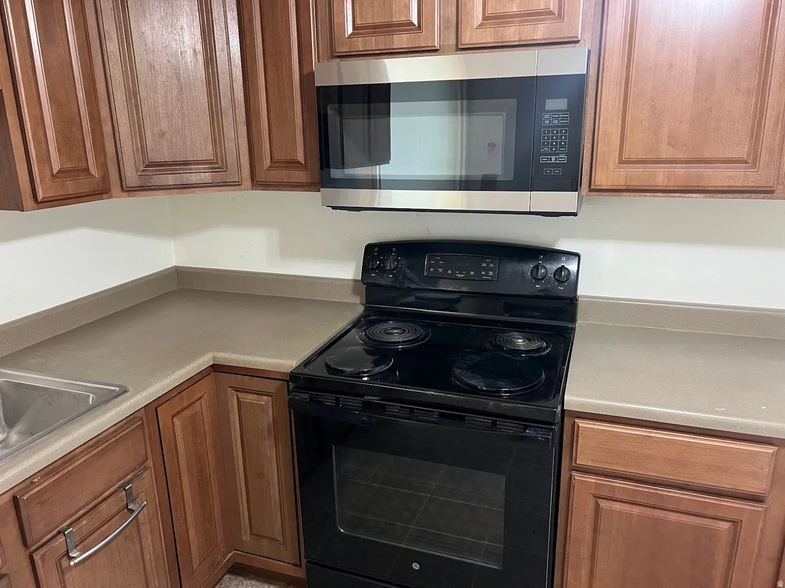Kitchen with black / electric stove, stainless steel microwave, wood finish cabinets, and light countertops