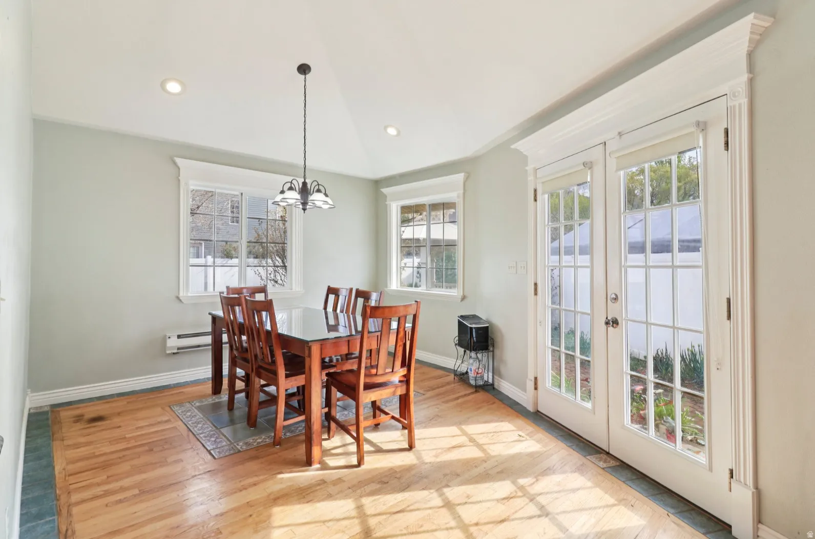 Dining room with french doors, vaulted ceiling, light wood-type flooring, suspended lighting, and a baseboard heating unit