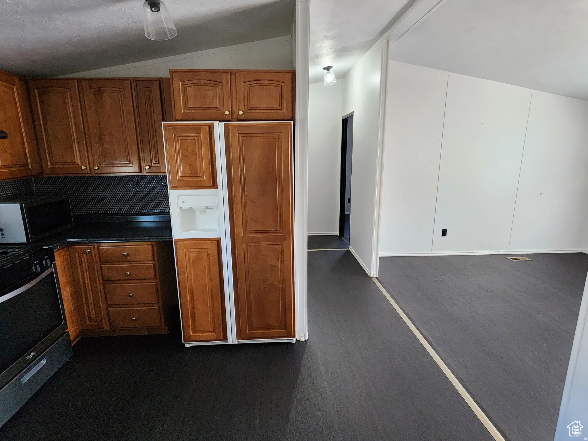 Kitchen with stainless steel appliances, dark countertops, lofted ceiling, and wood finish cabinetry