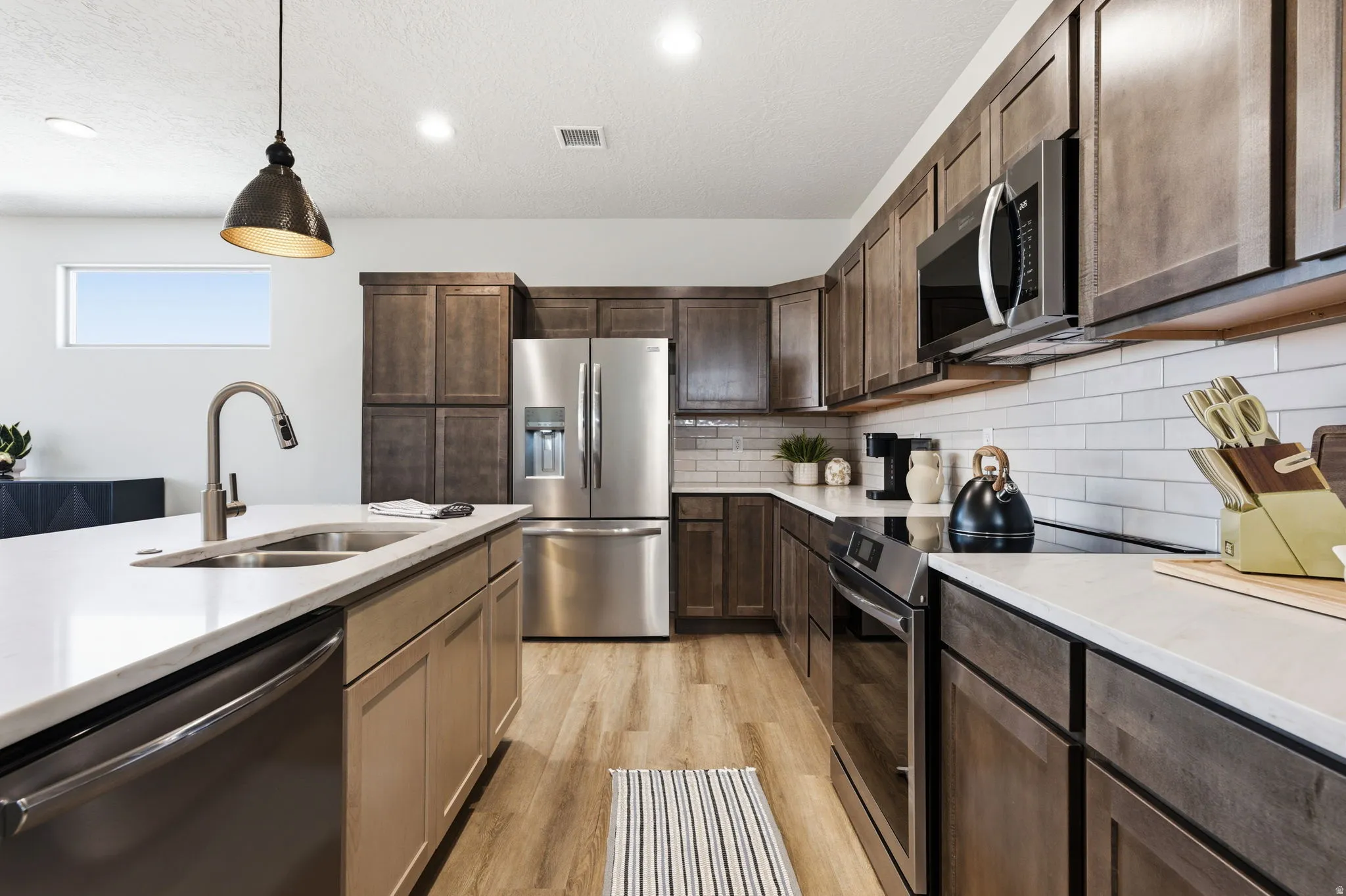 Kitchen featuring stainless steel appliances, hanging light fixtures, light wood-style flooring, light stone countertops, and a textured ceiling