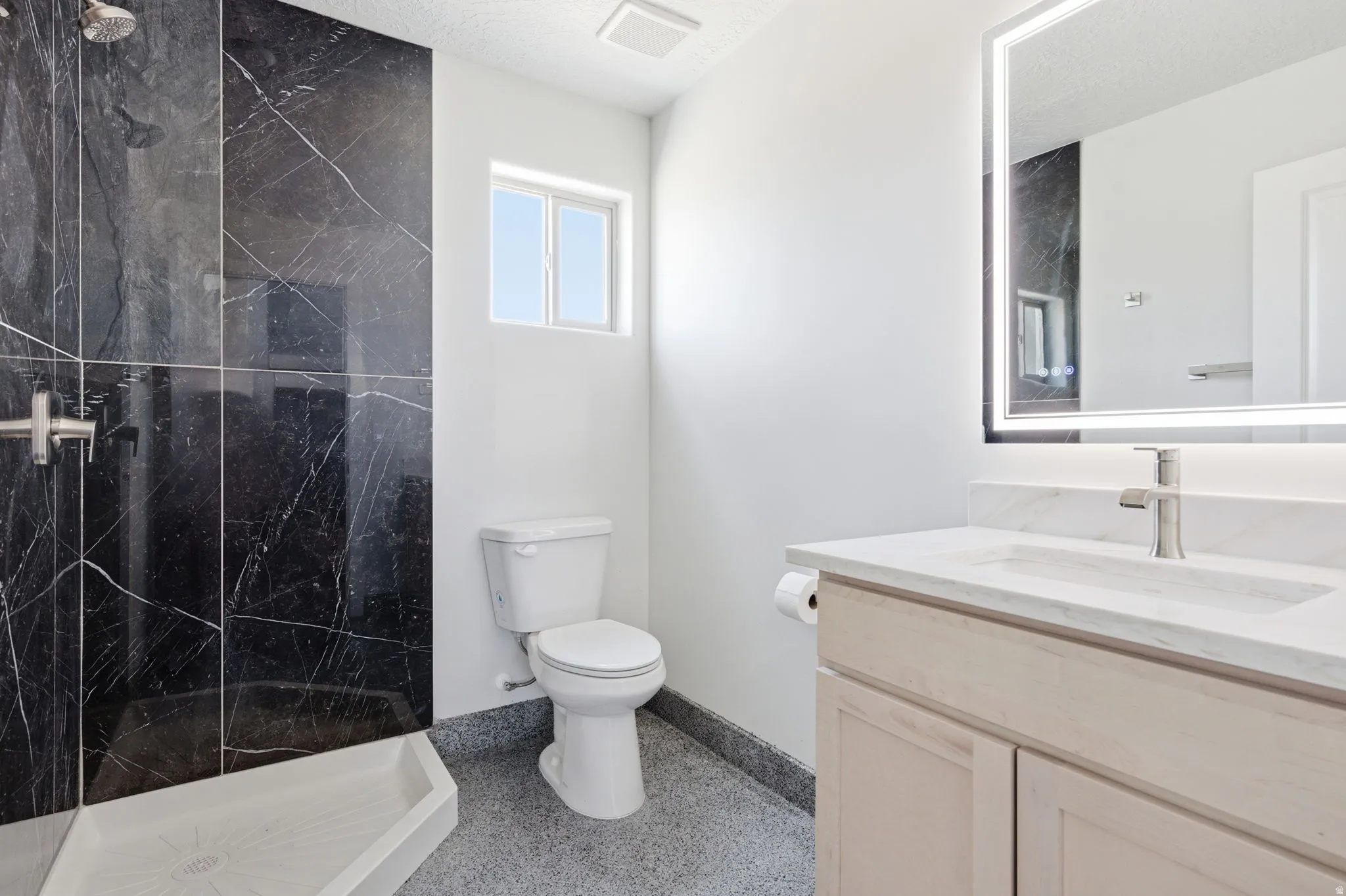 Full bathroom featuring vanity, a marble finish shower, and dark aggregate flooring