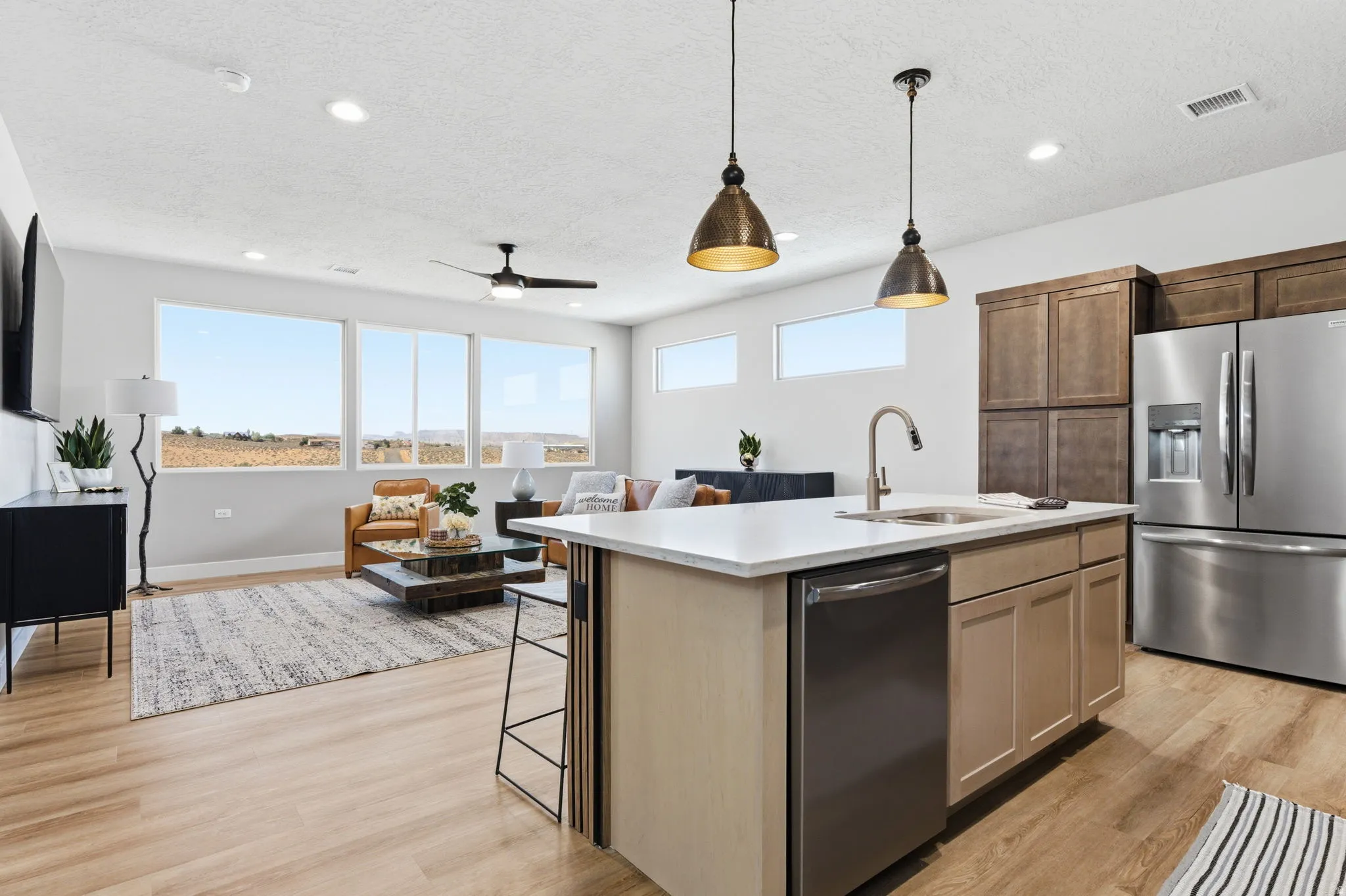 Kitchen featuring open floor plan, stainless steel appliances, a kitchen island with sink, decorative light fixtures, and light wood-style floors