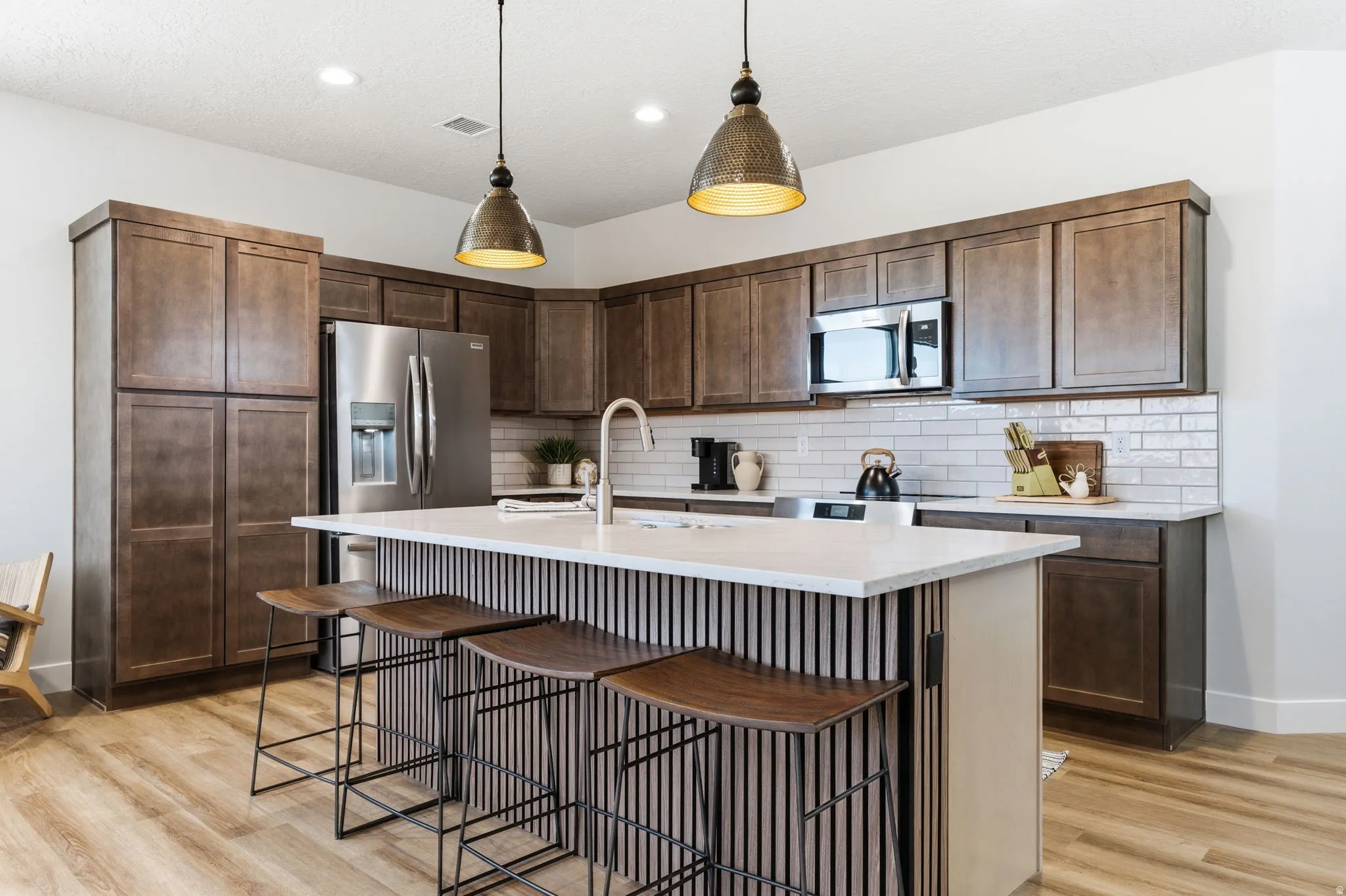 Kitchen with a breakfast bar, a center island with sink, decorative light fixtures, and dark wood finish cabinetry