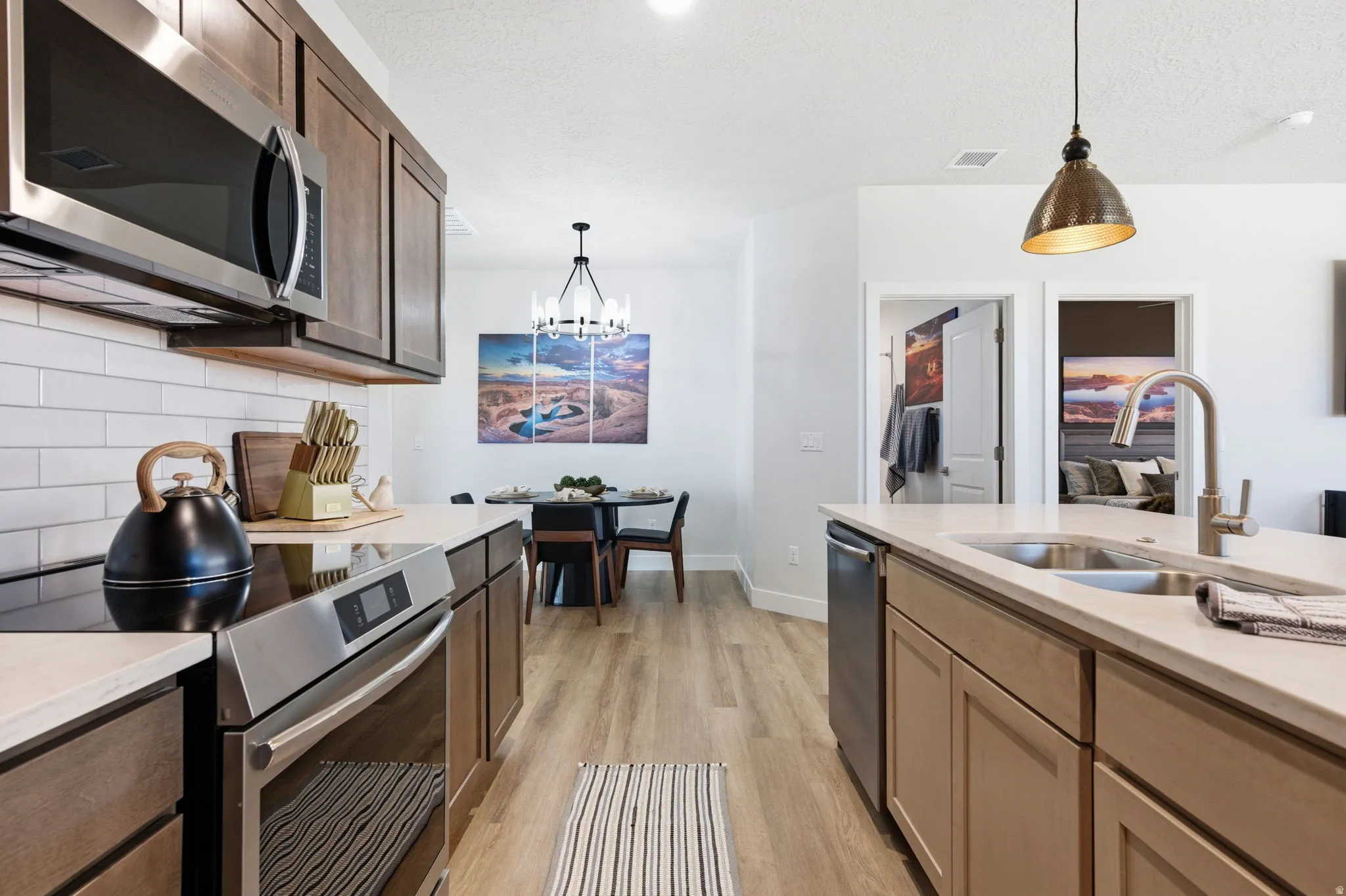 Kitchen with stainless steel appliances, light wood finished floors, light stone counters, a chandelier, and decorative backsplash