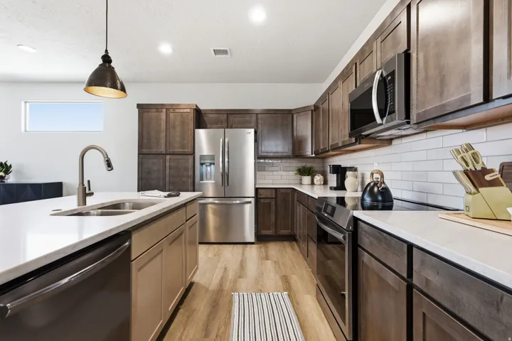 Kitchen featuring stainless steel appliances, hanging light fixtures, light wood-style flooring, light stone countertops, and a textured ceiling