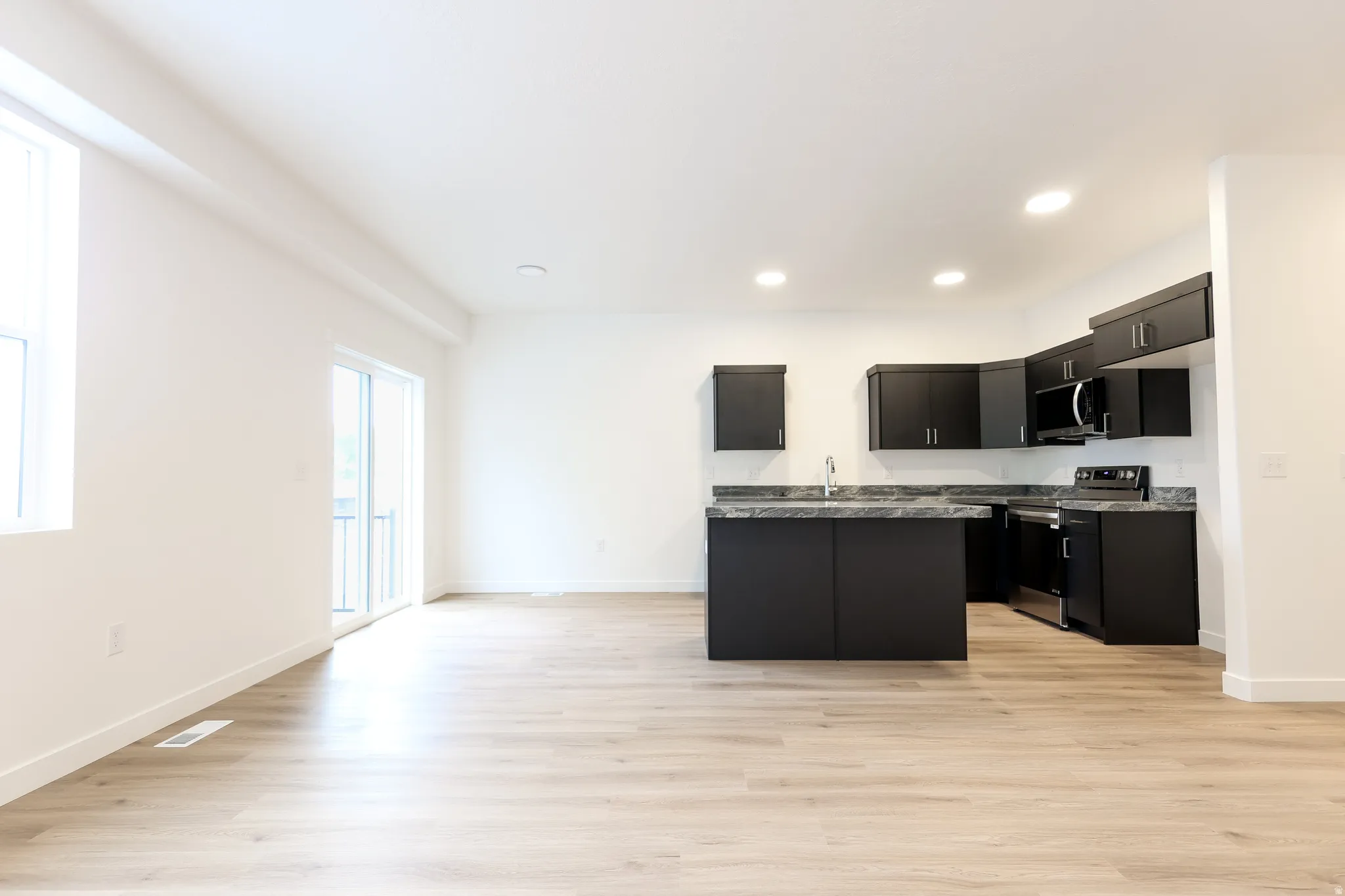 Kitchen with dark cabinetry, a kitchen island, stainless steel appliances, light wood-style floors, and recessed lighting