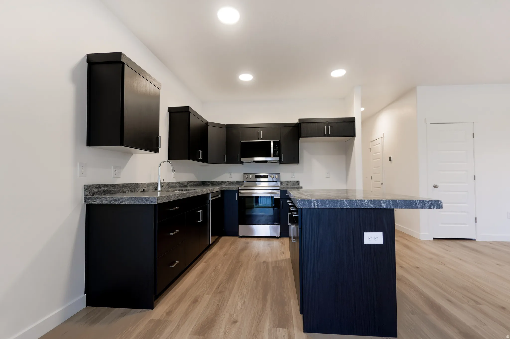 Kitchen with dark cabinets, stainless steel appliances, a center island, and light wood-style floors