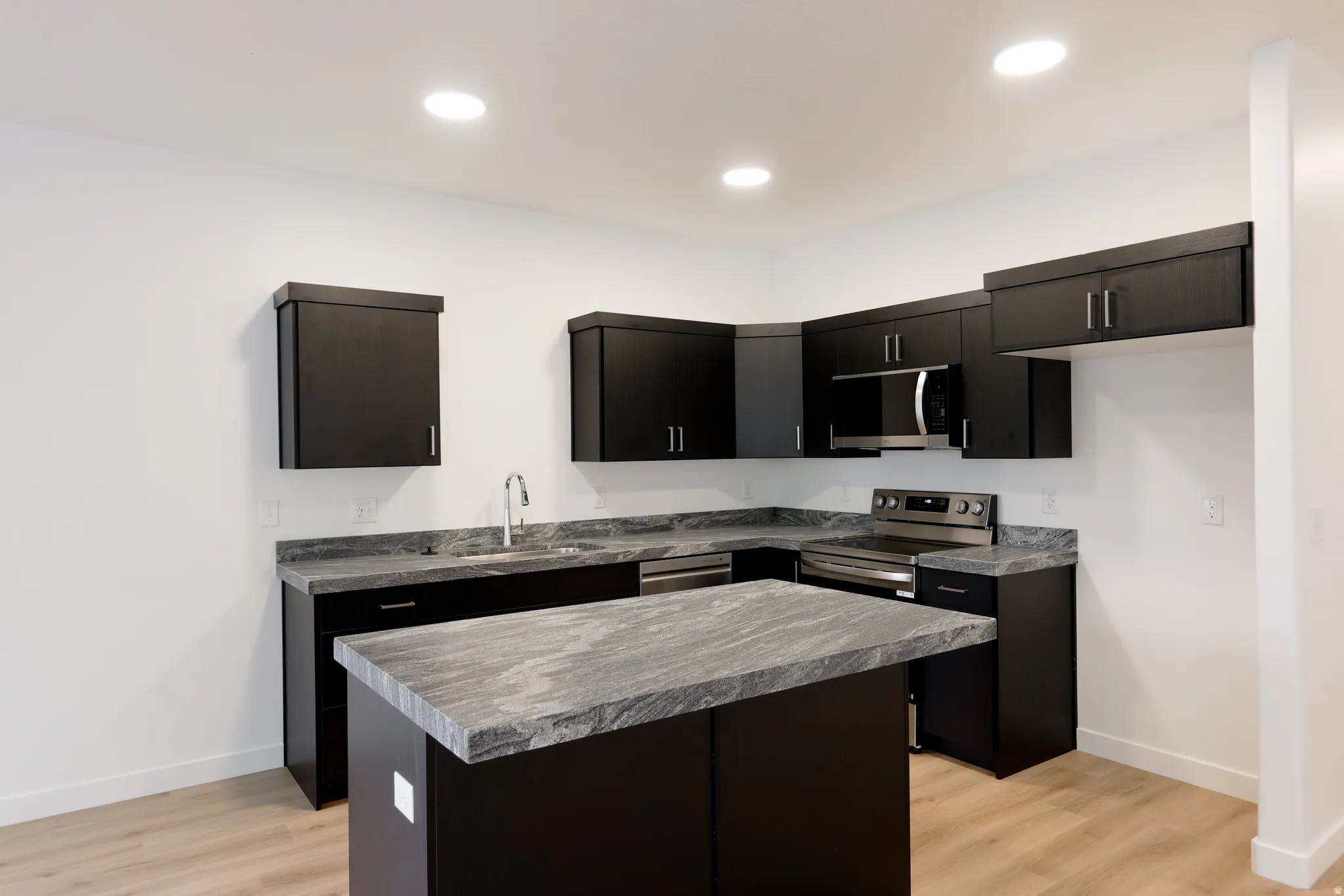 Kitchen featuring dark cabinets, a kitchen island, light wood-style floors, stainless steel appliances, and dark countertops