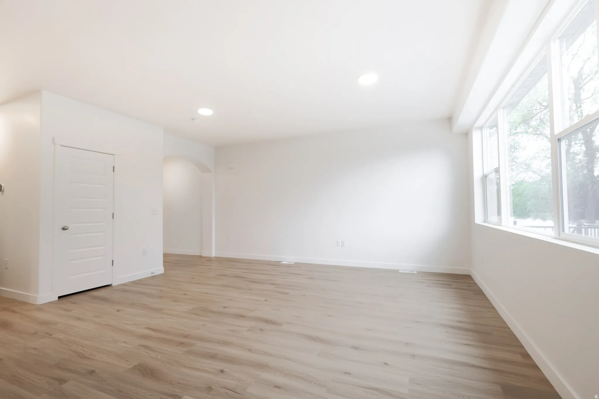 Unfurnished room featuring arched walkways, light wood-style flooring, and recessed lighting