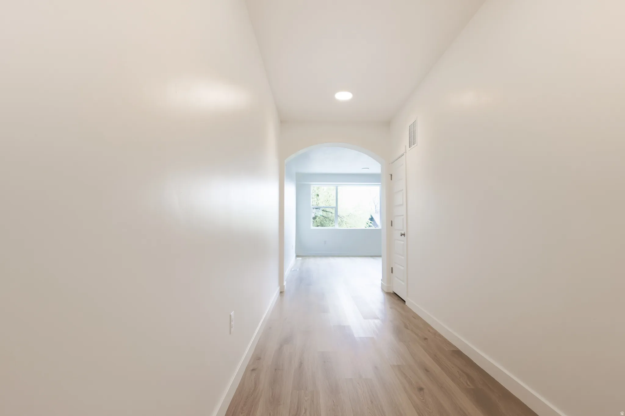 Hall featuring arched walkways, light wood-style floors, and recessed lighting