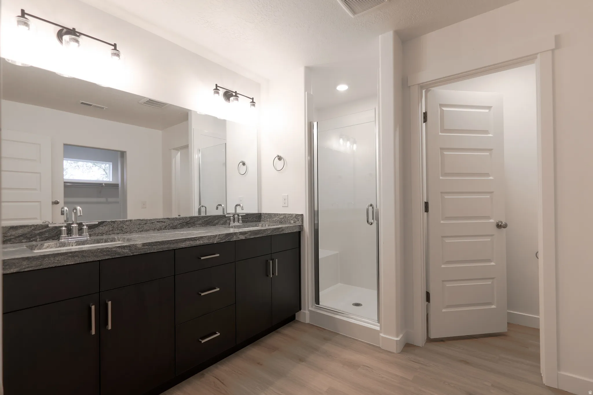 Bathroom with double vanity, a stall shower, light wood-type flooring, and a textured ceiling