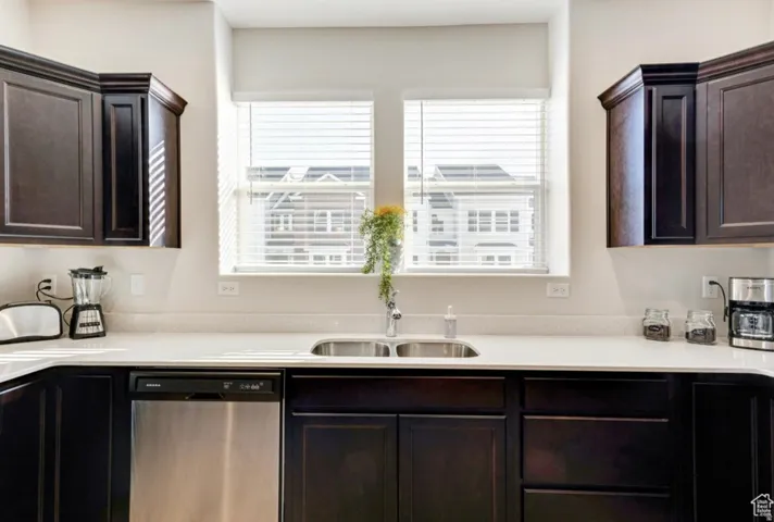 Kitchen featuring stainless steel dishwasher, dark wood finish cabinets, healthy amount of natural light, and light stone countertops