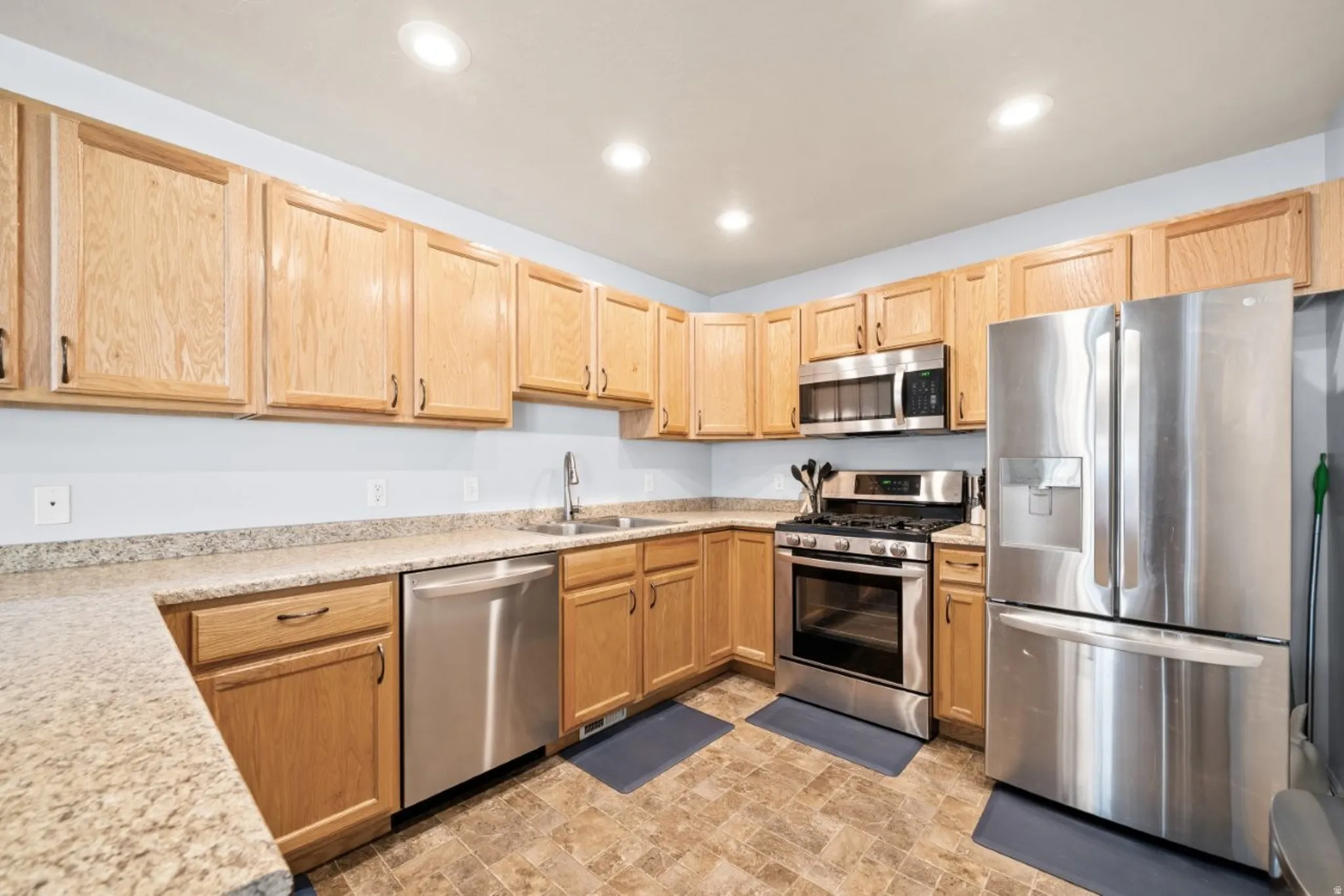 Kitchen featuring stainless steel appliances, light wood finish cabinetry, stone finish flooring, recessed lighting, and light stone counters