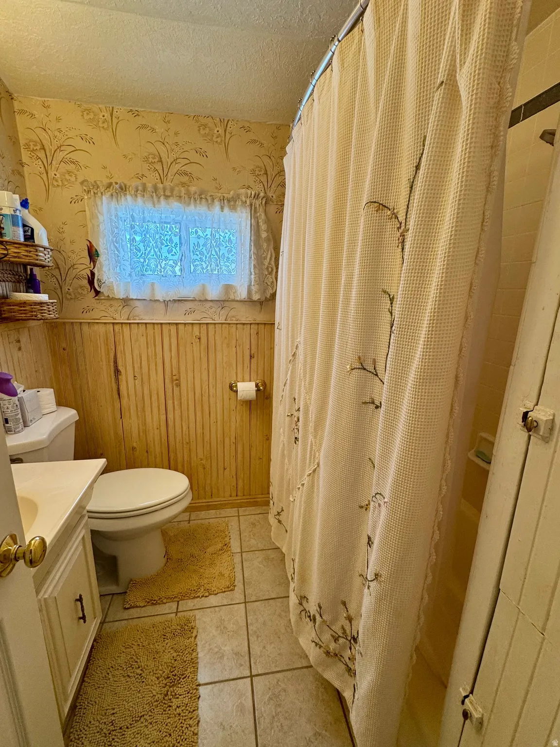 Bathroom featuring a wainscoted wall, vanity, a textured ceiling, wooden walls, and wallpapered walls