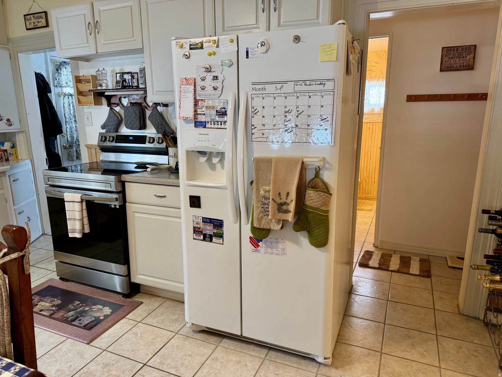 Kitchen with electric stove, white fridge with ice dispenser, white cabinetry, and light tile patterned floors