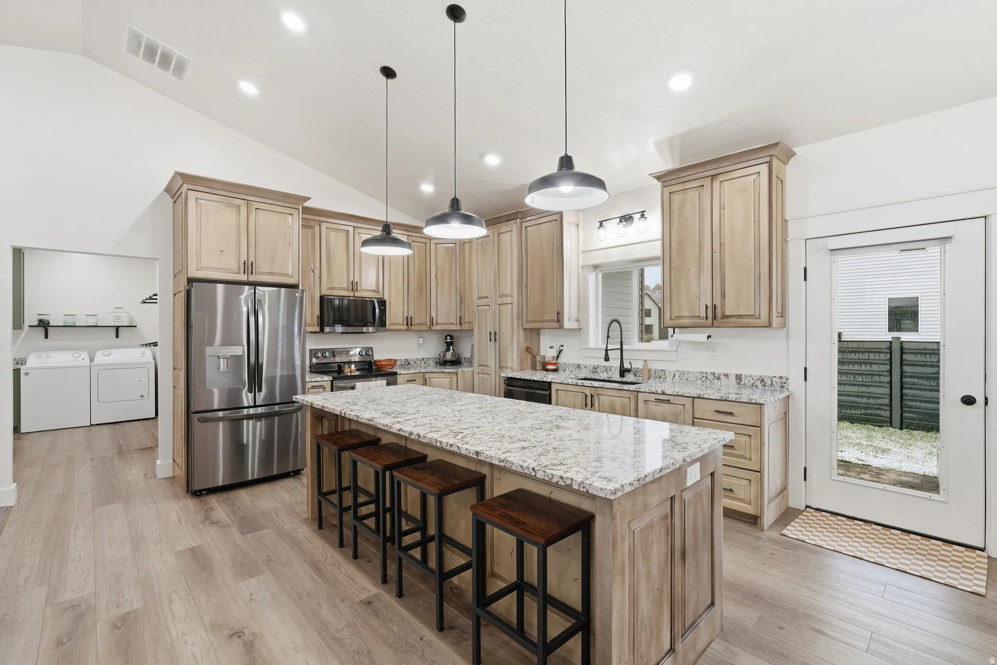 Kitchen with lofted ceiling, black appliances, washing machine and dryer, a kitchen breakfast bar, and light wood-style floors