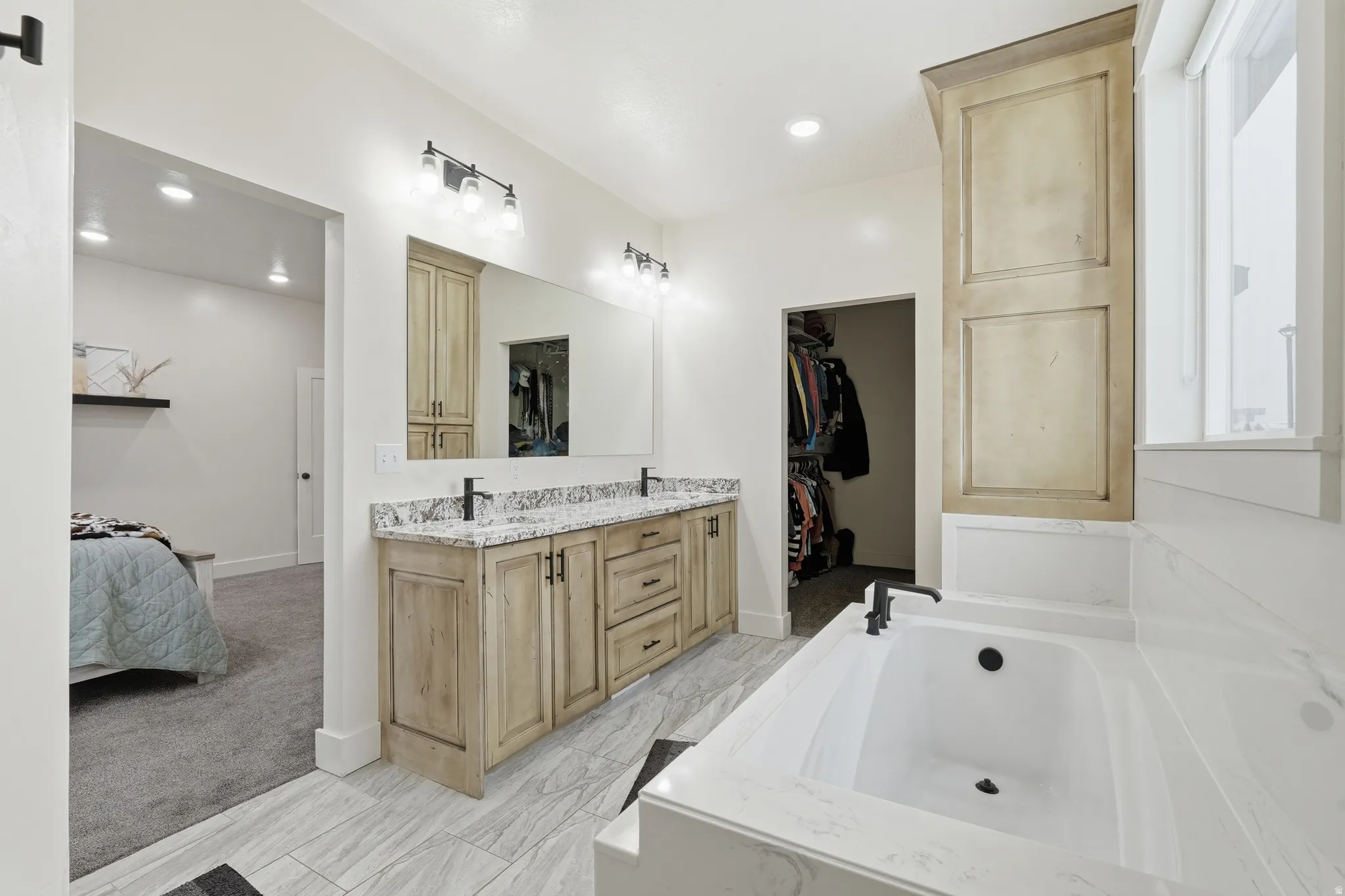 Bathroom featuring connected bathroom, a walk in closet, double vanity, a bath, and light marble finish flooring