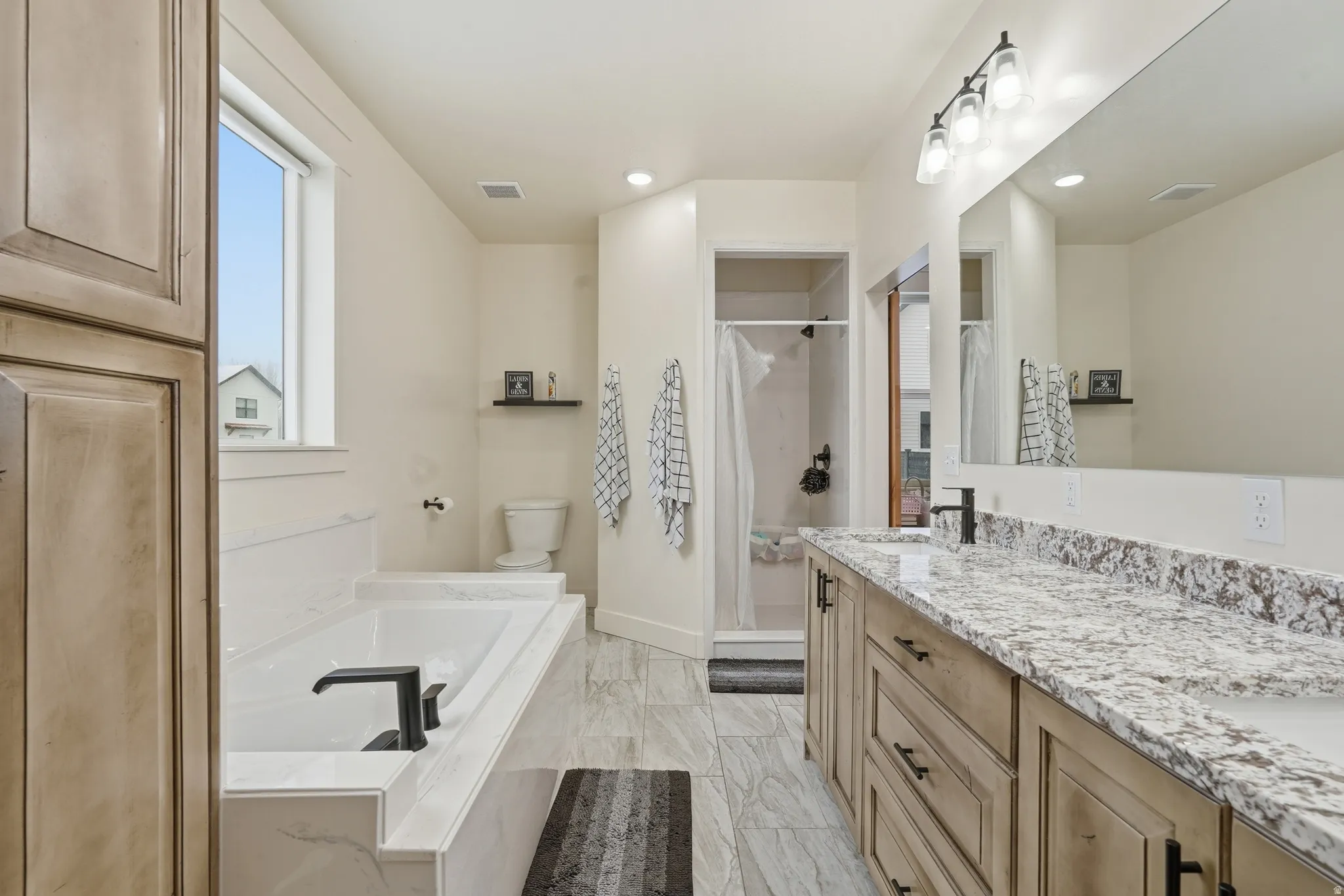Bathroom featuring double vanity, a garden tub, a stall shower, light marble finish flooring, and recessed lighting