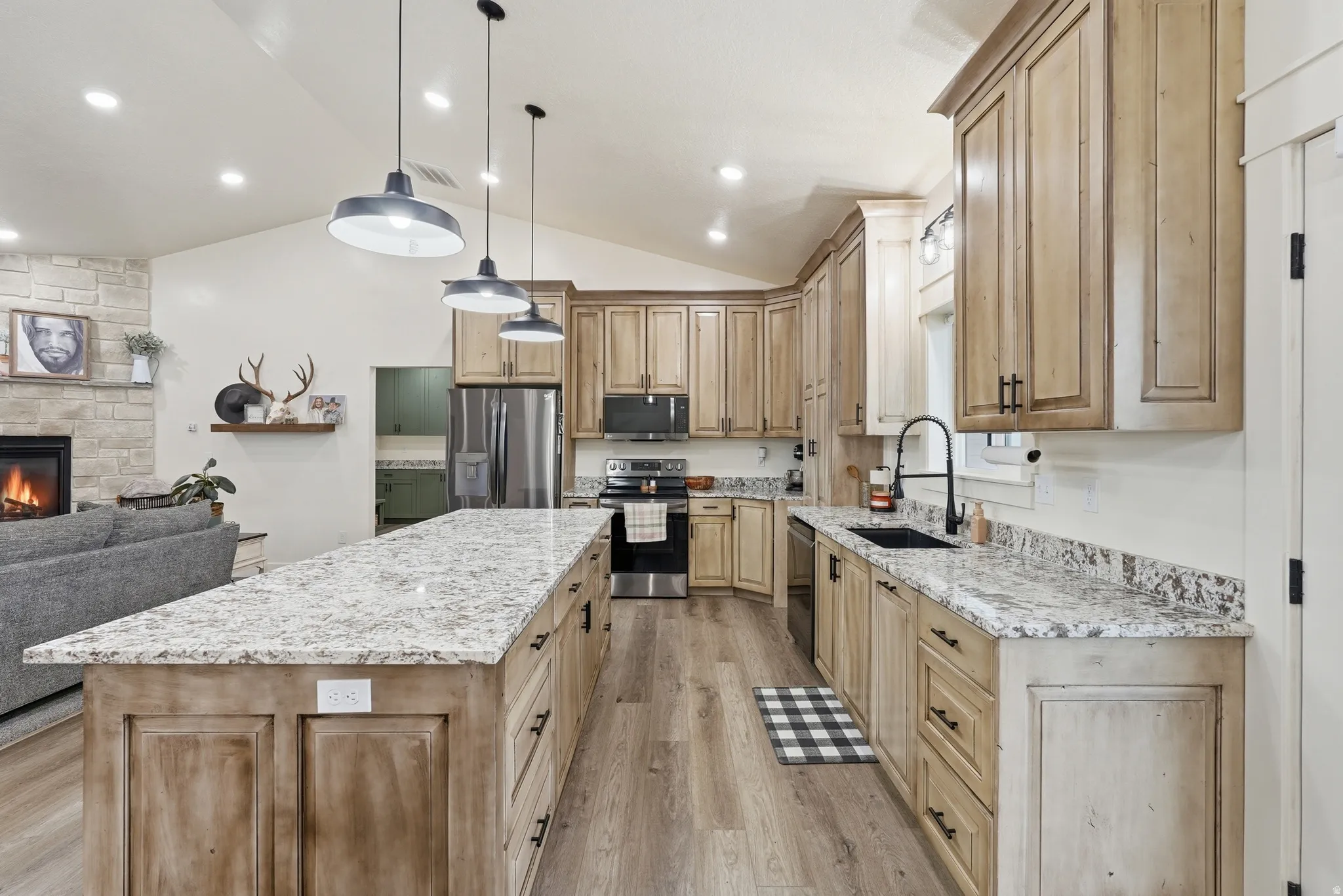 Kitchen with open floor plan, light stone counters, lofted ceiling, light wood finish cabinetry, and stainless steel appliances
