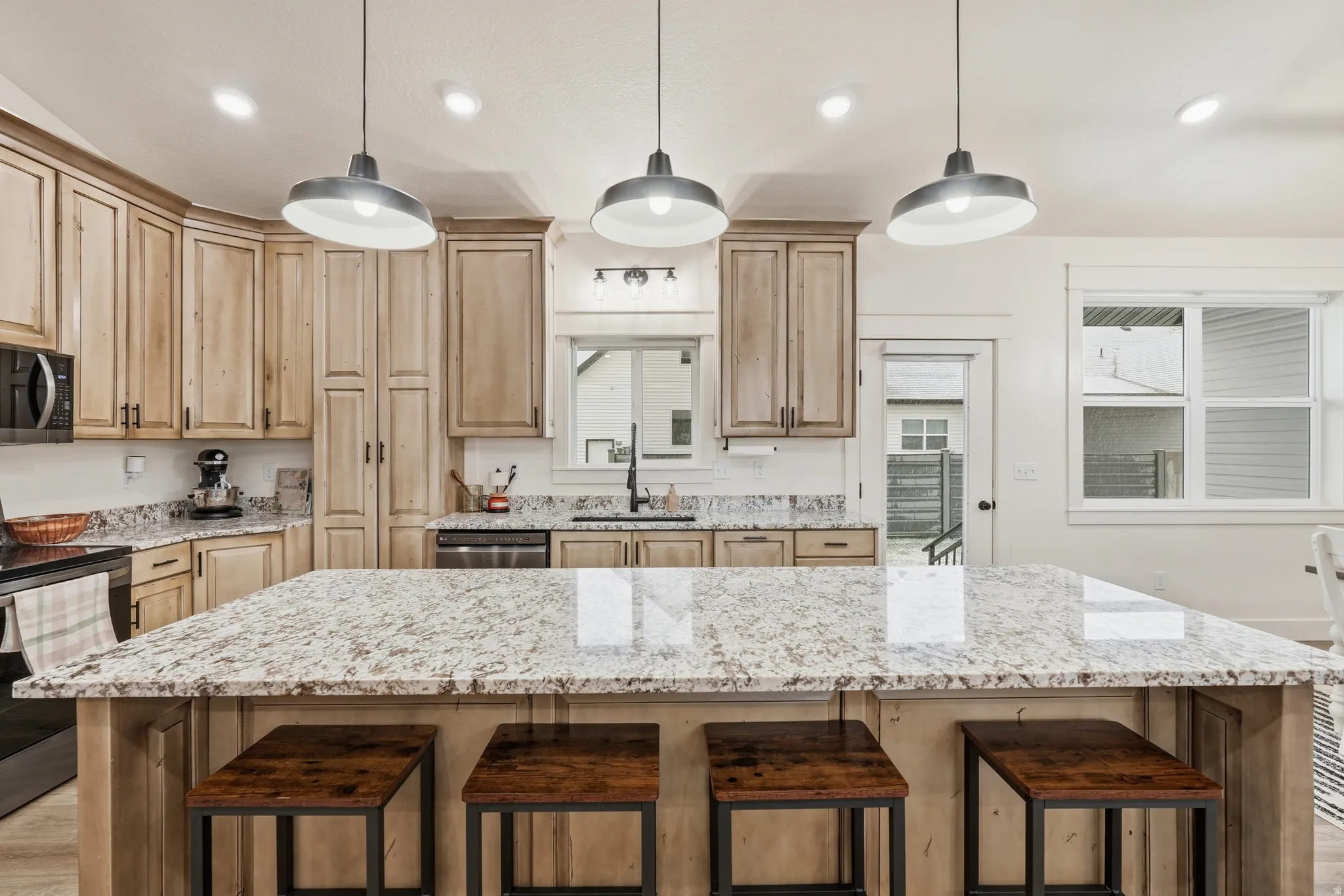 Kitchen featuring light wood finish cabinets, black appliances, a kitchen breakfast bar, and light stone counters