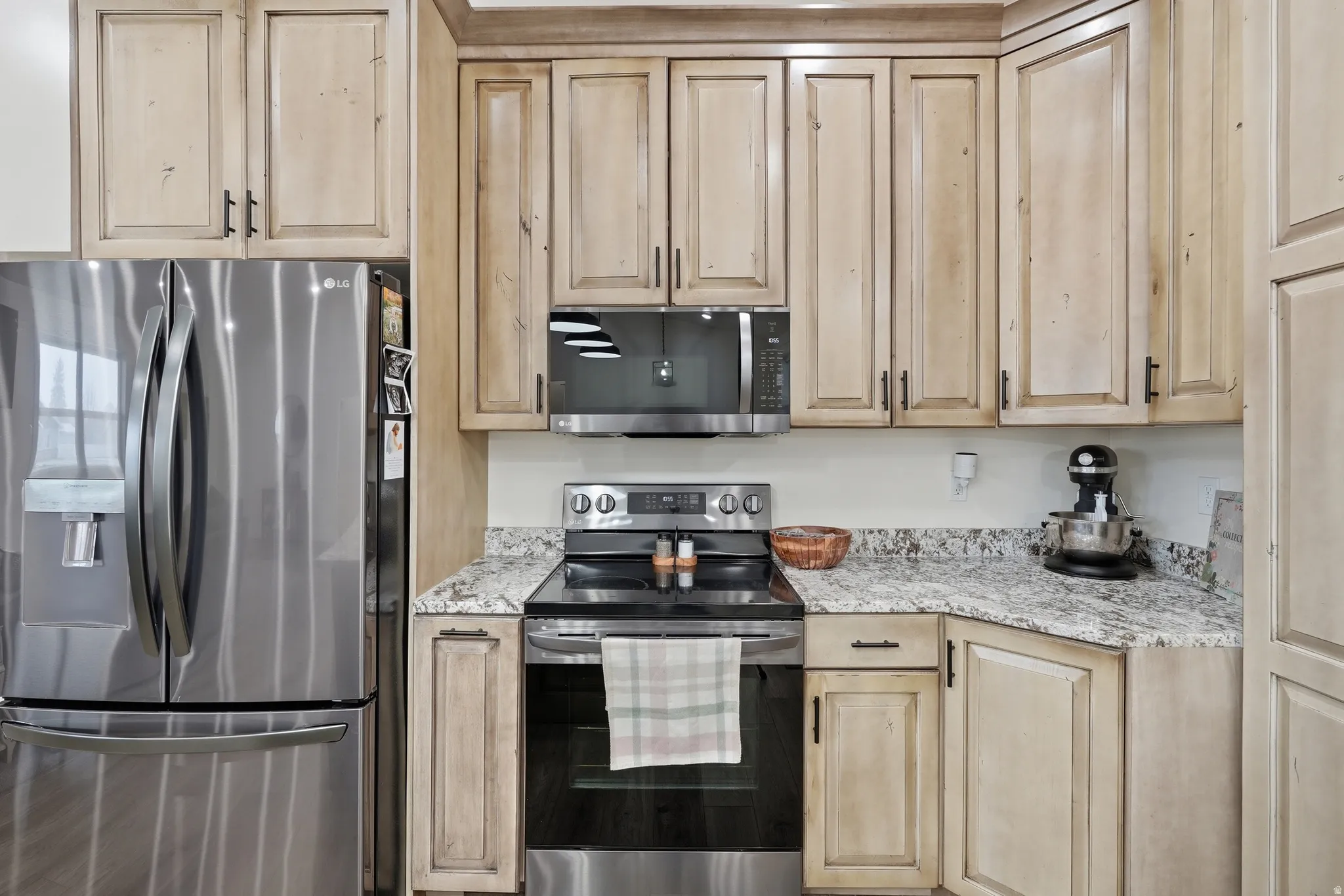 Kitchen featuring stainless steel appliances, light stone countertops, and light wood finish cabinets