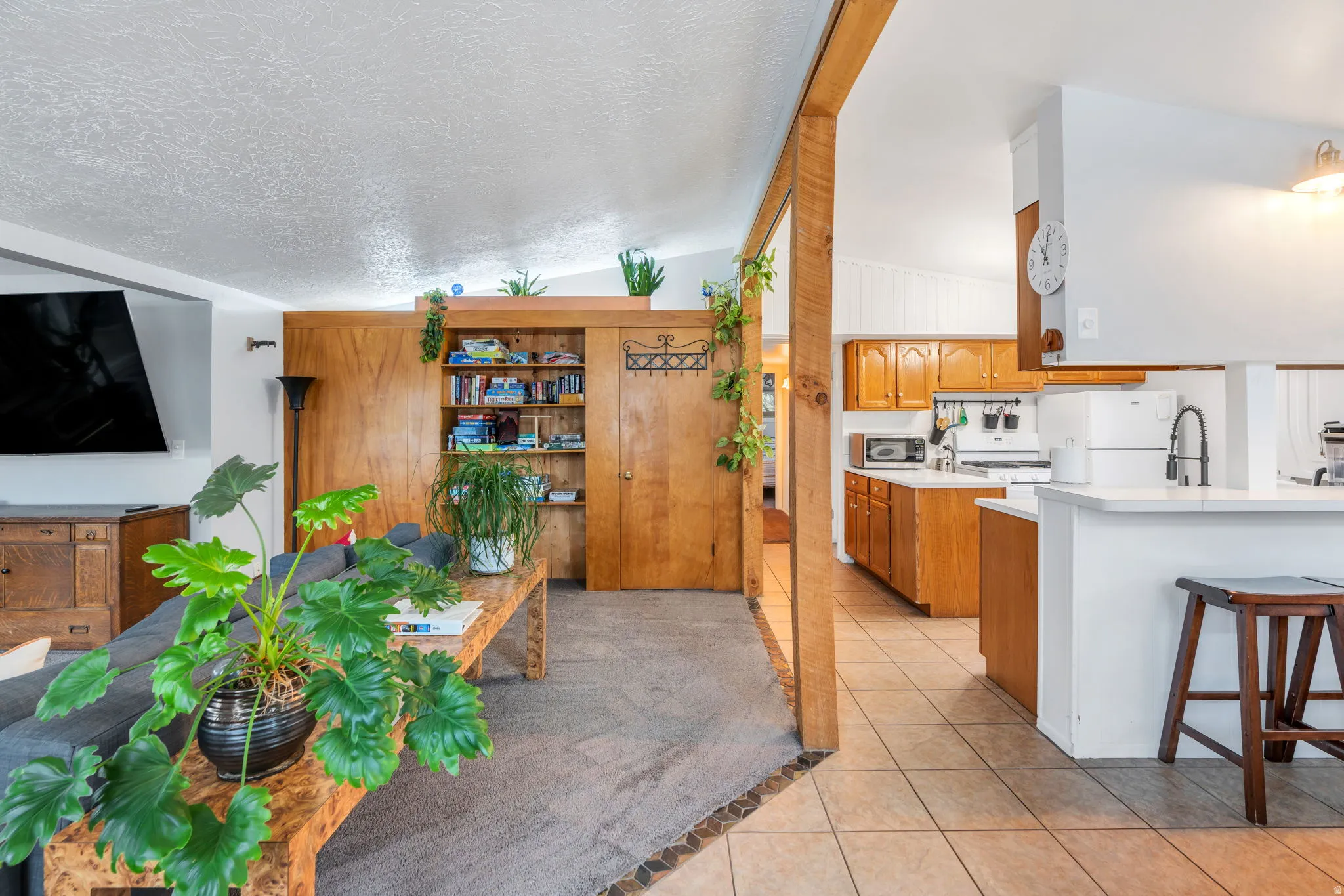 Kitchen with light countertops, light tile patterned floors, wood finish cabinets, white appliances, and a kitchen breakfast bar