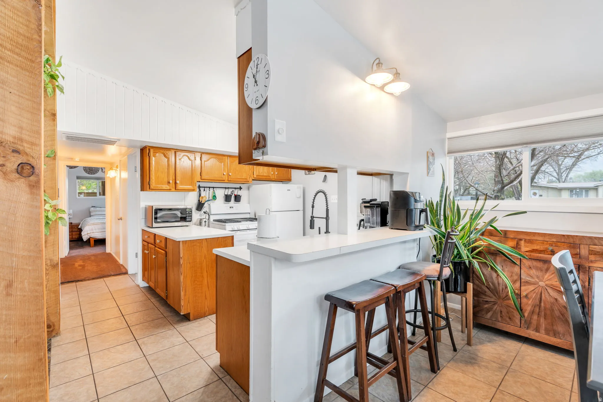 Kitchen featuring wood finish cabinets, light tile patterned flooring, light countertops, white appliances, and a kitchen bar