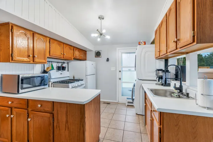 Kitchen featuring wood finish cabinets, a peninsula, light countertops, washer / dryer, and white appliances