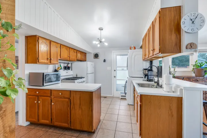 Kitchen featuring a peninsula, wood finish cabinets, light countertops, hanging lights, and washer / clothes dryer