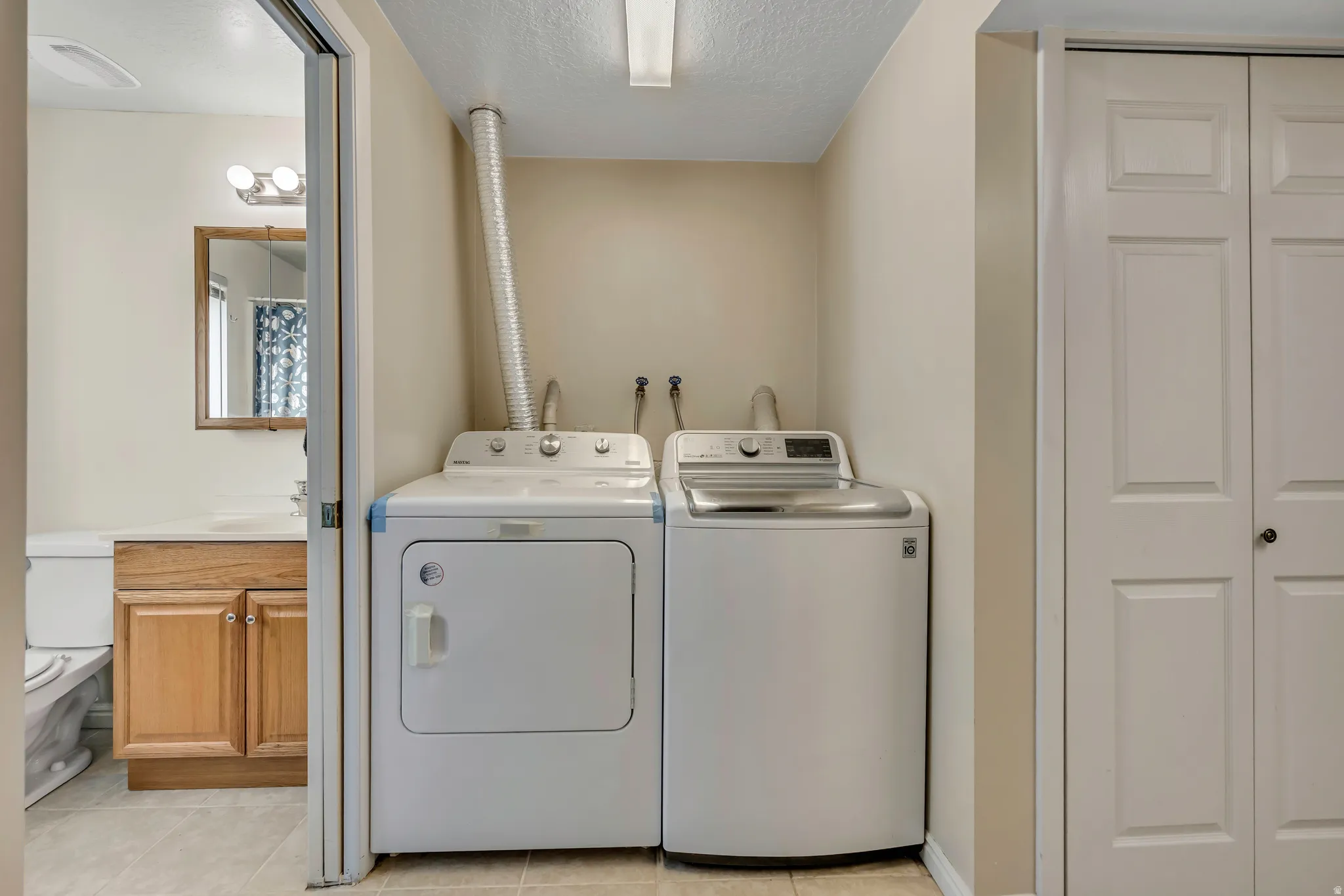 Laundry area featuring a textured ceiling, washer and dryer, and light tile patterned floors