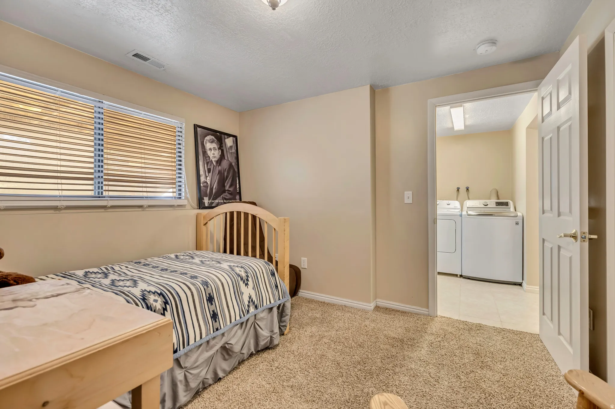 Bedroom with light carpet, washer and dryer, and a textured ceiling