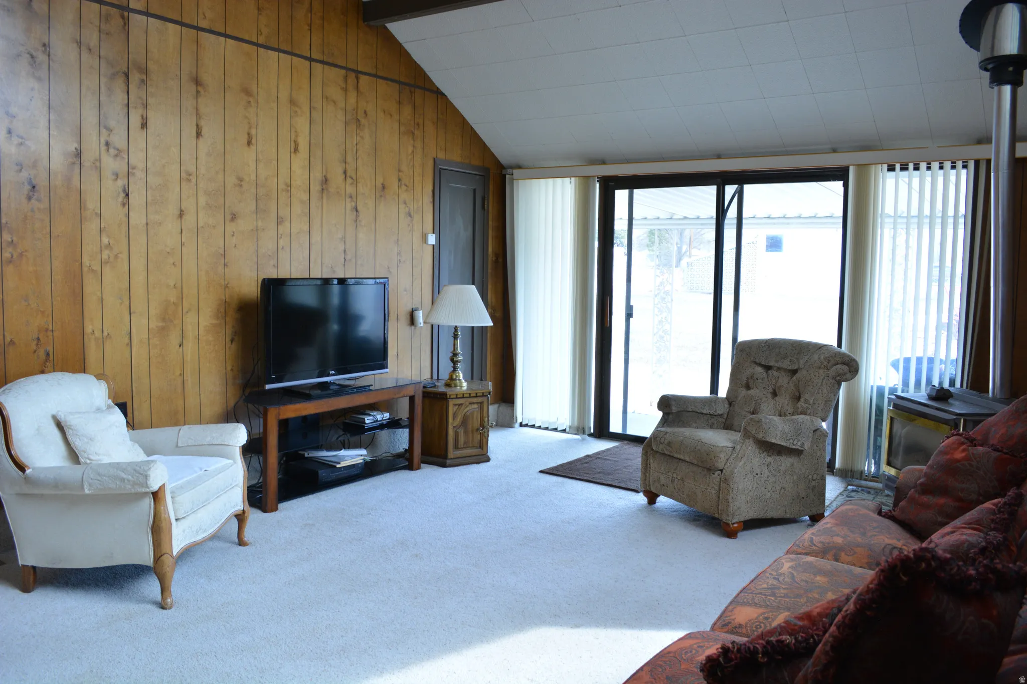 Living area featuring carpet floors, wooden walls, and vaulted ceiling with beams