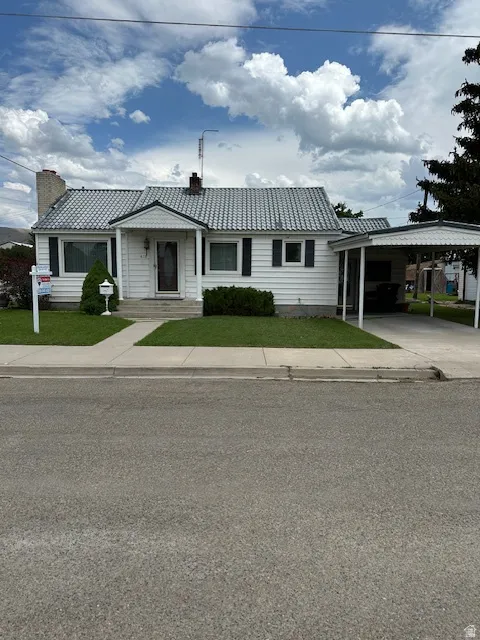 Ranch-style house featuring a front yard, a chimney, a carport, and driveway