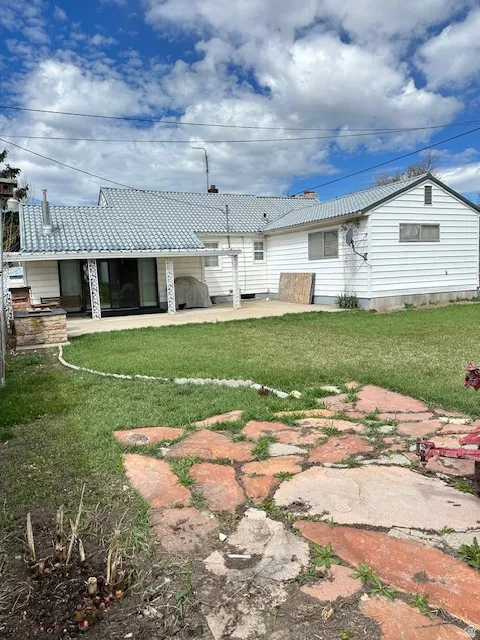 Rear view of house featuring a lawn, a patio area, and a metal roof