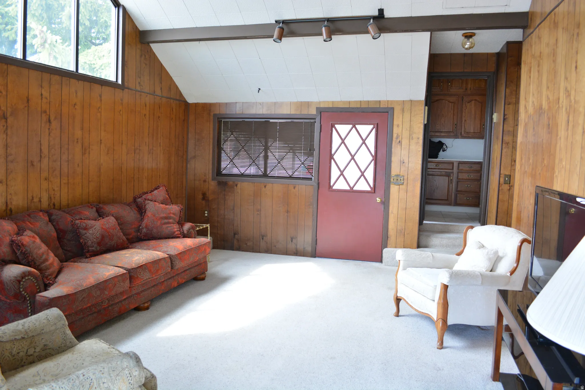 Living room featuring wood walls, carpet, lofted ceiling with beams, and track lighting