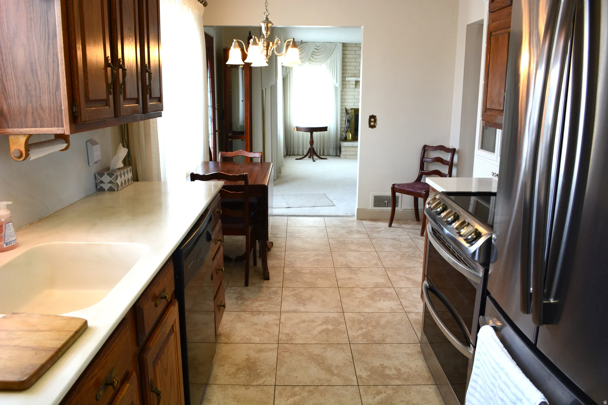Kitchen featuring stainless steel appliances, light countertops, hanging lights, light tile patterned floors, and dark wood finish cabinetry
