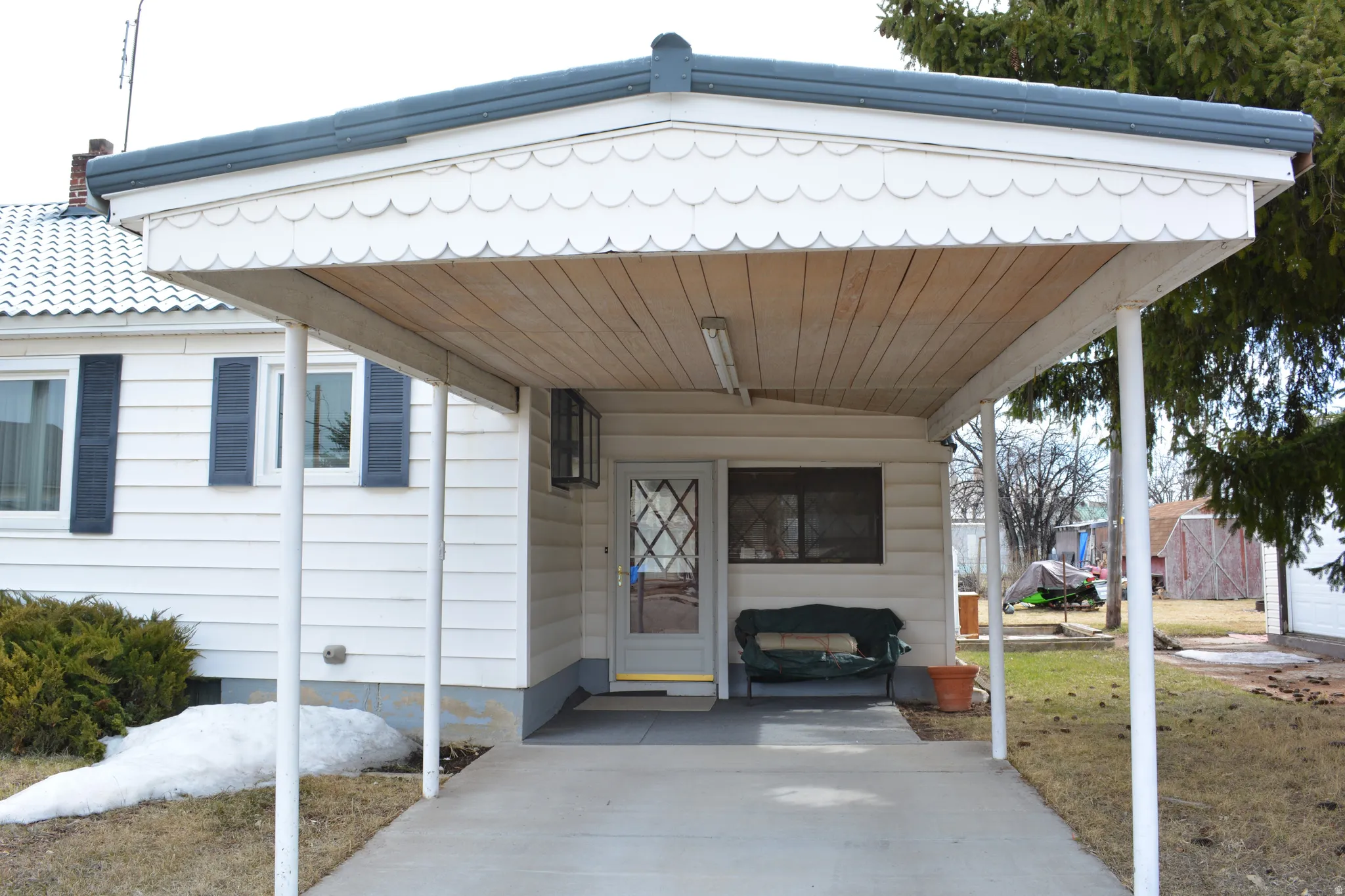 View of exterior entry featuring an attached carport, a yard, and a porch